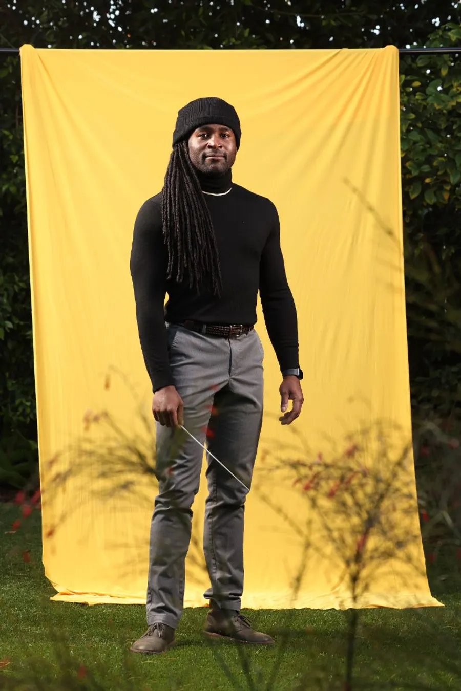 Alexander Blake standing in front of yellow backdrop with a baton.